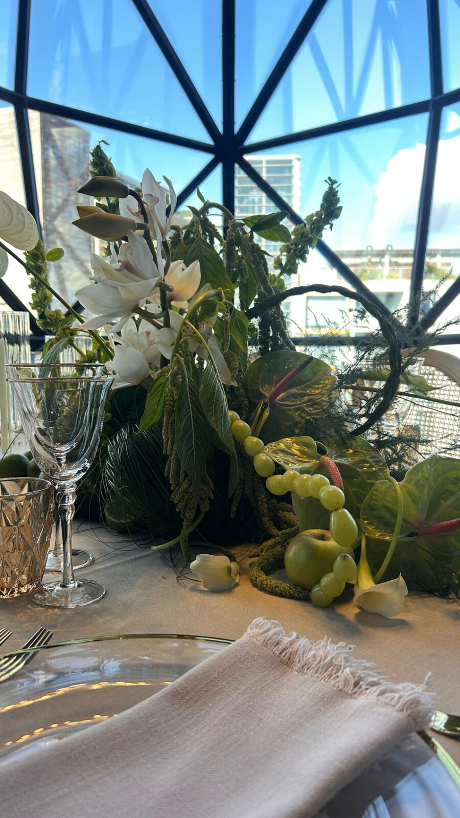 White orchid and anthurium centrepiece with green fruit on a rooftop table